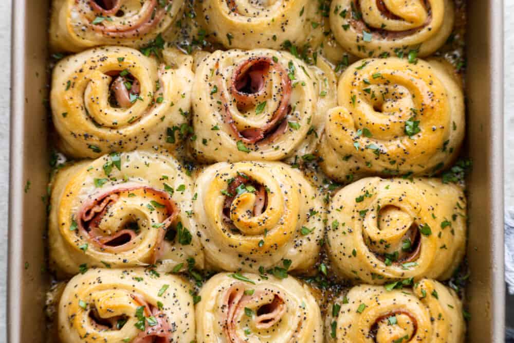 Hot Ham and Swiss Pinwheels have smoked ham and melty swiss cheese that are rolled up in croissantย dough and are brushed with a buttery garlic poppyseed topping! The perfect insanely delicious quick and easy dinner or appetizer! The top view of pinwheels in a baking sheet.