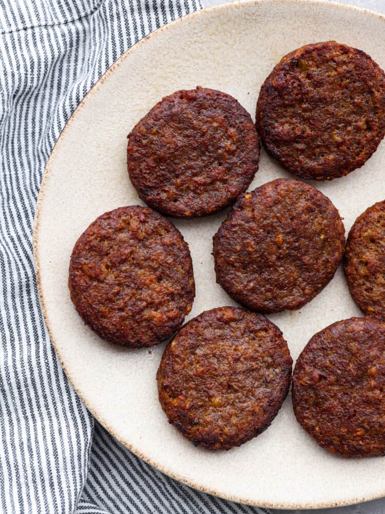 For a quick and delicious breakfast, try making frozen sausage patties in the air fryer! In less than 10 minutes they turn tender and juicy, perfect for adding to your favorite English muffins! Cooked sausage patties on a white plate.