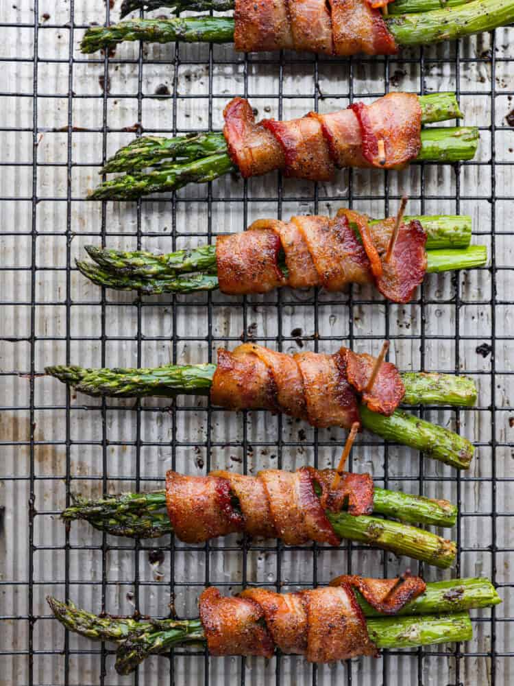 Bacon wrapped asparagus is a smoky and savory side dish that will be a staple for mealtime. Each bundle is glazed with maple syrup for caramelized flavor you wonโt be able to get enough of! Bacon-wrapped asparagus on a cooling rack.
