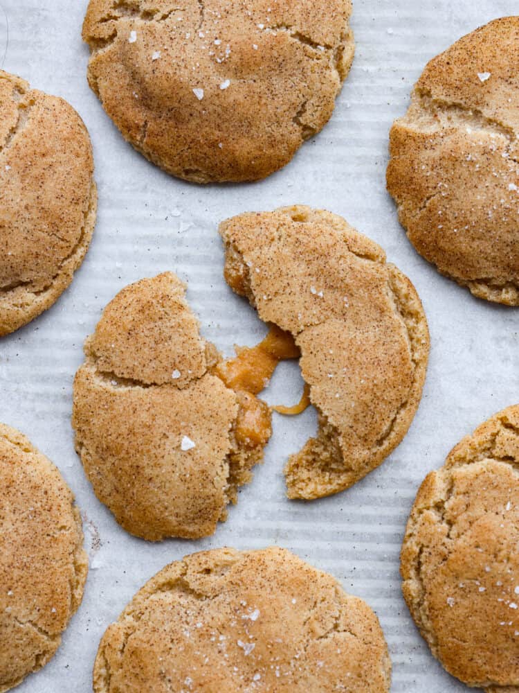 This recipe takes snickerdoodles to the next level! Made with brown butter and a salted caramel core, each bite is a sweet and nutty dream! Top-down view of brown butter salted caramel snickerdoodles. One is broken in half, revealing a gooey caramel center.
