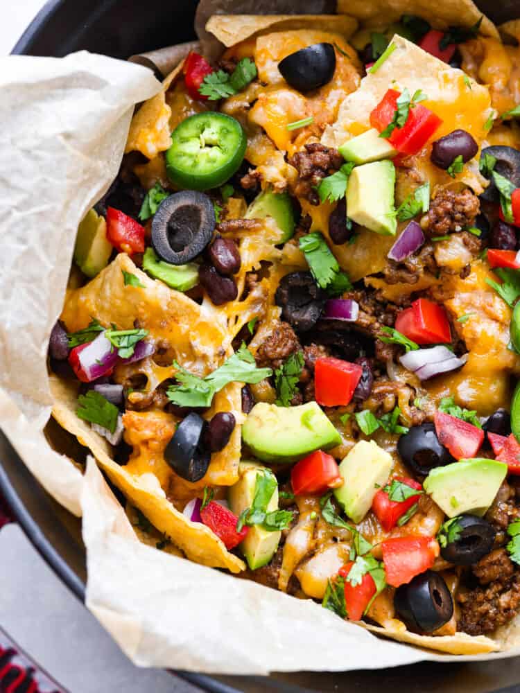 These campfire nachos are the ultimate outdoor comfort food! Packed with layers of seasoned ground beef, refried beans, and gooey cheese, these nachos are then topped with your favorite veggies and will be a new summertime favorite! A closeup of campfire nachos.