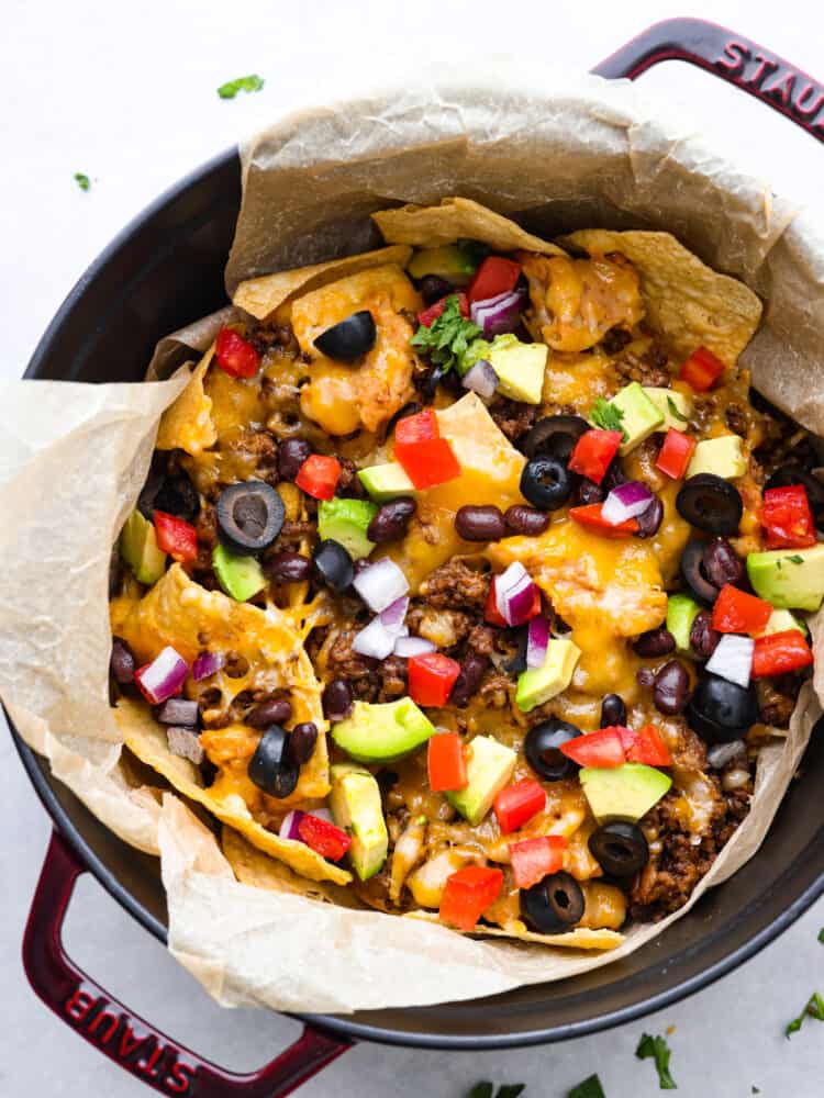 These campfire nachos are the ultimate outdoor comfort food! Packed with layers of seasoned ground beef, refried beans, and gooey cheese, these nachos are then topped with your favorite veggies and will be a new summertime favorite! The top view of campfire nachos that are cooked.