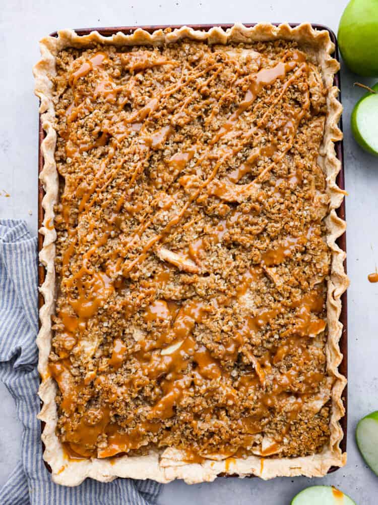 Caramel Apple Slab Pie has a thin and flaky melt-in-your-mouth crust that is topped with juicy apples and a crisp topping. It is drizzled in homemade caramel and perfect for feeding a crowd! The top view of a bakes caramel apple slab pie.