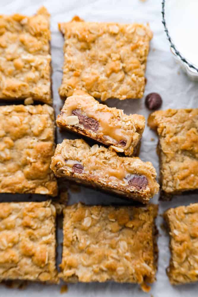 This recipe for Carmelitas is a divine dessert that combines layers of buttery oats, gooey caramel, and rich semisweet chocolate. With a perfect balance of sweetness and texture, these bars are a heavenly treat that will satisfy any sweet tooth. a zoomed in shot of Carmelitas on a pan with parchment paper.