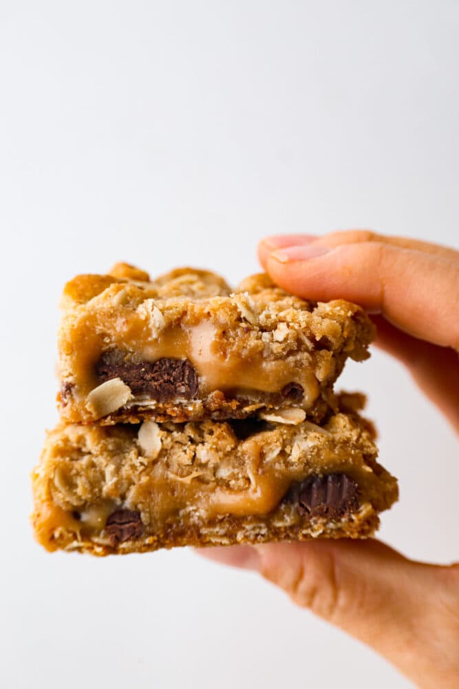 This recipe for Carmelitas is a divine dessert that combines layers of buttery oats, gooey caramel, and rich semisweet chocolate. With a perfect balance of sweetness and texture, these bars are a heavenly treat that will satisfy any sweet tooth. 2 Carmelitas being held in a stack.
