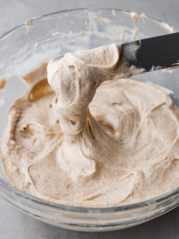 Whip up this simple cinnamon cream cheese frosting in less than 5 minutes! It's velvety smooth and once you add it to your cake or cupcakes for a delightful treat, everyone will be asking for seconds. A knife being dipped into a bowl with cinnamon cream cheese frosting.
