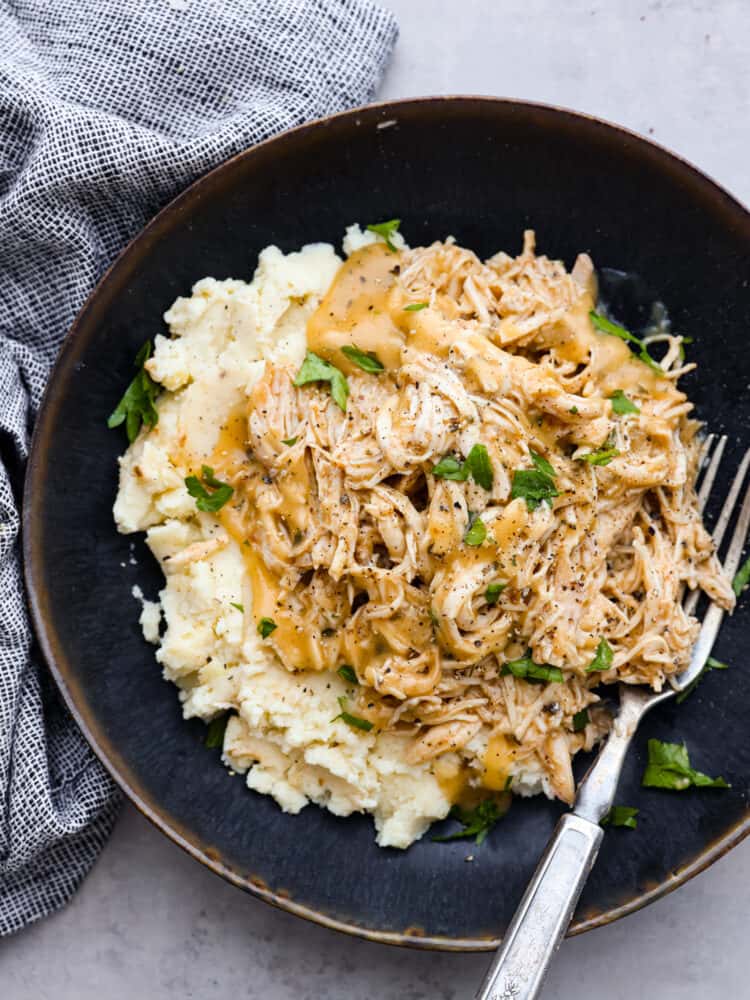 Whip up a comforting meal with this delicious Crockpot Chicken and Gravy recipe. Cooked to perfection in the slow cooker, the result is tender, juicy chicken smothered in a rich gravy, making it the perfect companion to rice or potatoes for a hearty and satisfying dinner! Chicken and gravy garnished with green onions on a plate with mashed potatoes.