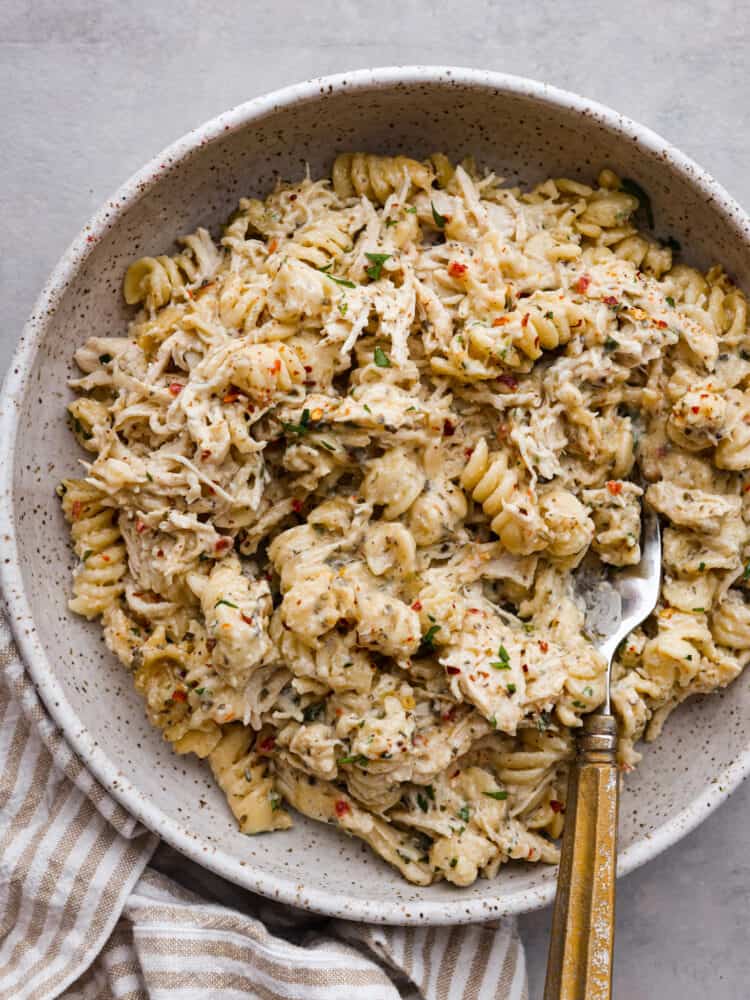If you're looking for a knockout dinner that the whole family will love, this crockpot parmesan garlic chicken pasta is the recipe to try. It's so flavorful and satisfying, everyone will be licking their plates clean! It's easy, cheesy, and packed with mouthwatering garlic flavor. A serving of chicken pasta in a gray speckled bowl.