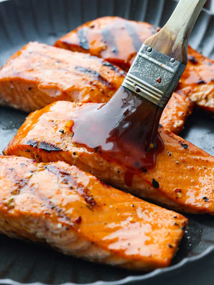 Looking to add a burst of flavor to your favorite dishes? With a perfect blend of heat and sweetness, this Firecracker Sauce will take any recipe to the next level. Whether you are using it as a basting sauce or a delightful dipping sauce, this is perfect for any meal! A basting brush basting salmon with firecracker sauce.