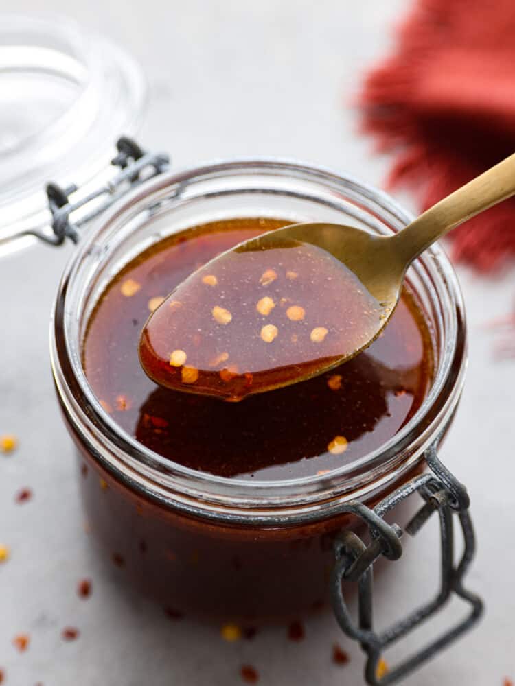 Looking to add a burst of flavor to your favorite dishes? With a perfect blend of heat and sweetness, this Firecracker Sauce will take any recipe to the next level. Whether you are using it as a basting sauce or a delightful dipping sauce, this is perfect for any meal! A clear jar of firecracker sauce iwht a gold spoon scooping some out.