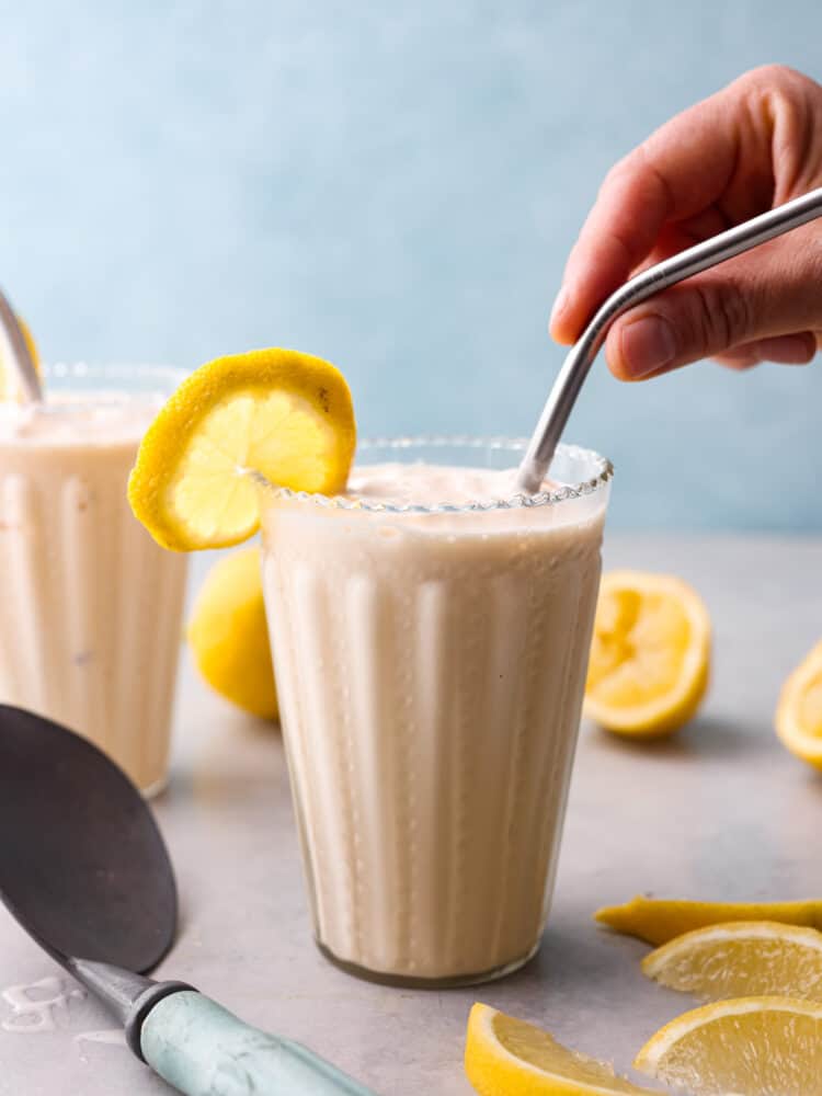 This Copycat Chick Fil A Frosted Lemonade is a delicious and creamy cold drink for the summer. This copycat frozen lemonade is so refreshing and perfect for hot days! The side view of a frosted lemonade with a hand putting a straw in the glass.