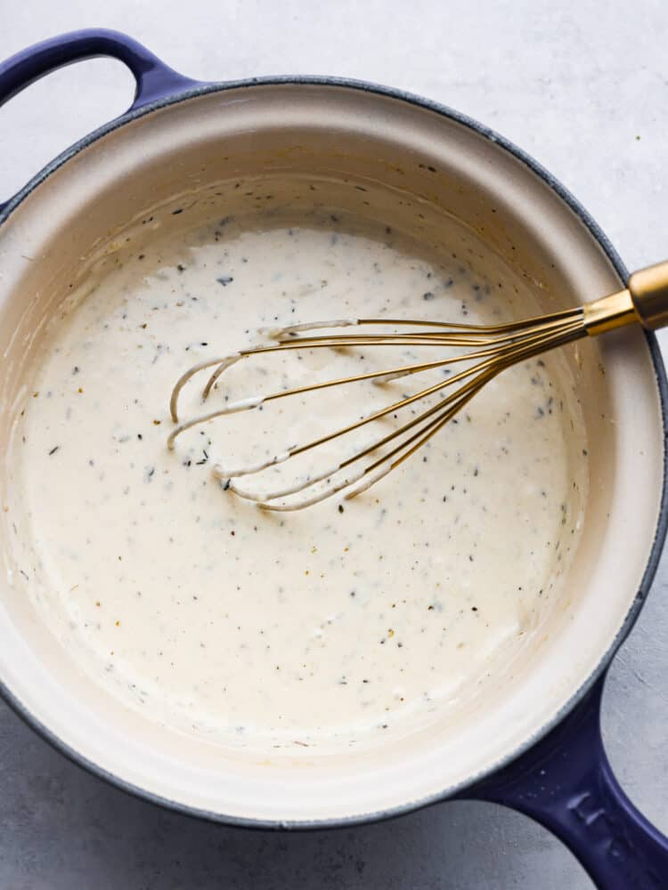 Garlic parmesan sauce is a copycat recipe from the famous Buffalo Wild Wings restaurant. This creamy garlic sauce is best known as a wing sauce, but it's perfect for pasta, on pizza, or used as a dipping sauce. Close overhead photo of garlic parmesan sauce in a blue saucepan being stirred with a gold whisk.