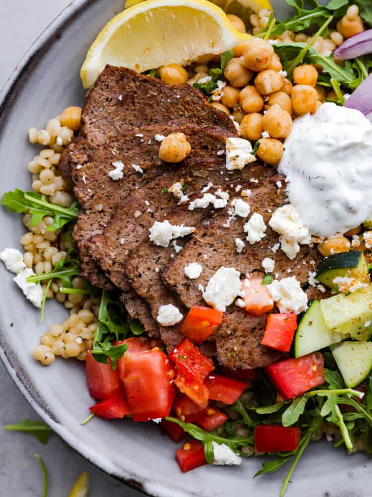 My easy-to-make gyro meat is perfectly seasoned and tender every time! Just like your favorite Mediterranean restaurant. Perfect for pitas, bowls, or platters with all your favorite toppings. Closeup of gyro meat, topped with feta cheese and tzatziki sauce.