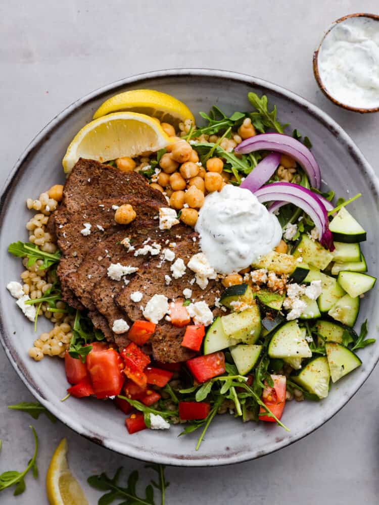 Take lunchtime up a notch with this incredible gyro bowl! It has tender gyro meat, fluffy couscous, crunchy veggies, and zesty tzatziki all in one bowl. Healthy, hearty, and totally irresistible. Top-down view of a gyro bowl.