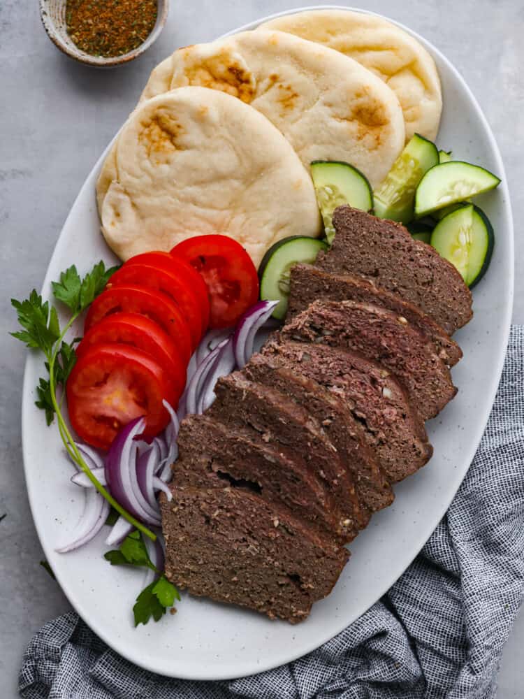 My easy-to-make gyro meat is perfectly seasoned and tender every time! Just like your favorite Mediterranean restaurant. Perfect for pitas, bowls, or platters with all your favorite toppings. Sliced gyro meat served with tomatoes, onions, cucumber, and pita bread.