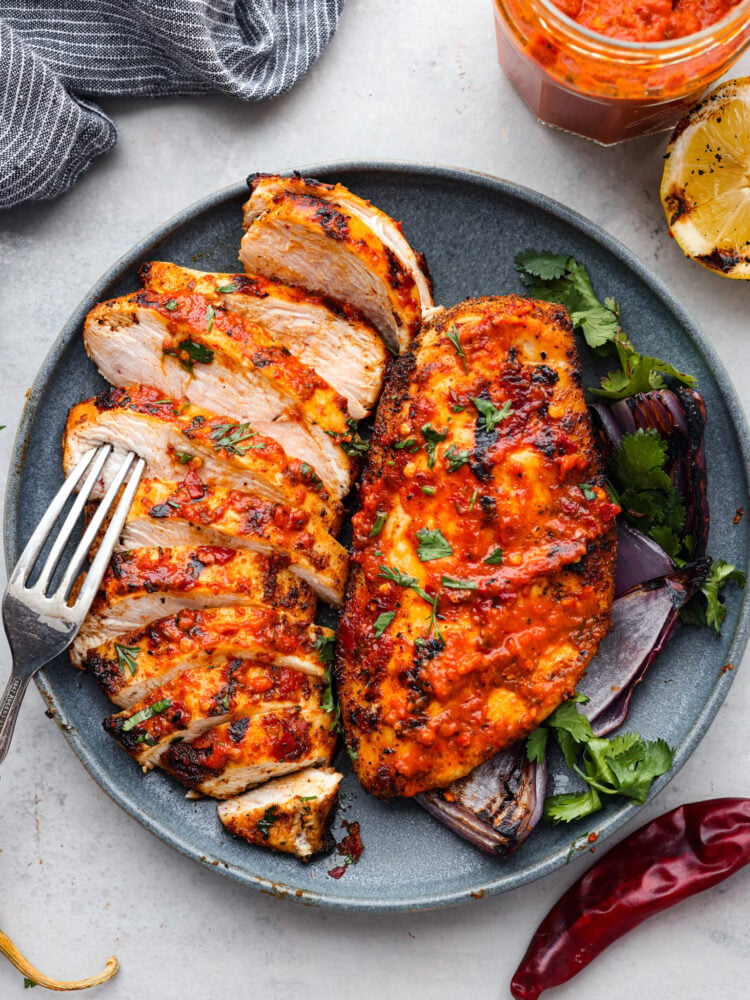 Harissa chicken is tender, juicy, and coated in a spicy, flavor-packed sauce that will leave your mouth watering. This easy and delicious North African dish is the perfect recipe to add to the dinner lineup this week! Harissa chicken sliced into pieces.