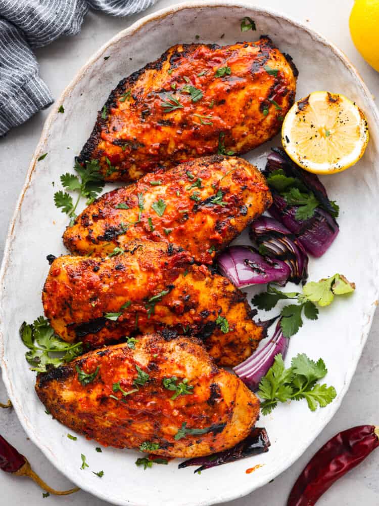 Harissa chicken is tender, juicy, and coated in a spicy, flavor-packed sauce that will leave your mouth watering. This easy and delicious North African dish is the perfect recipe to add to the dinner lineup this week! 4 pieces of harissa chicken served with vegetables and half of a lemon.