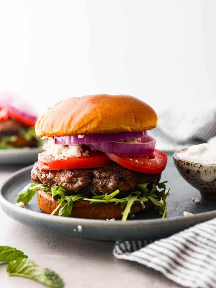 Make these amazing lamb burgers to add a Greek twist to your next summer barbecue! A lamb burger topped with tomatoes, onion, arugula, and feta cheese.