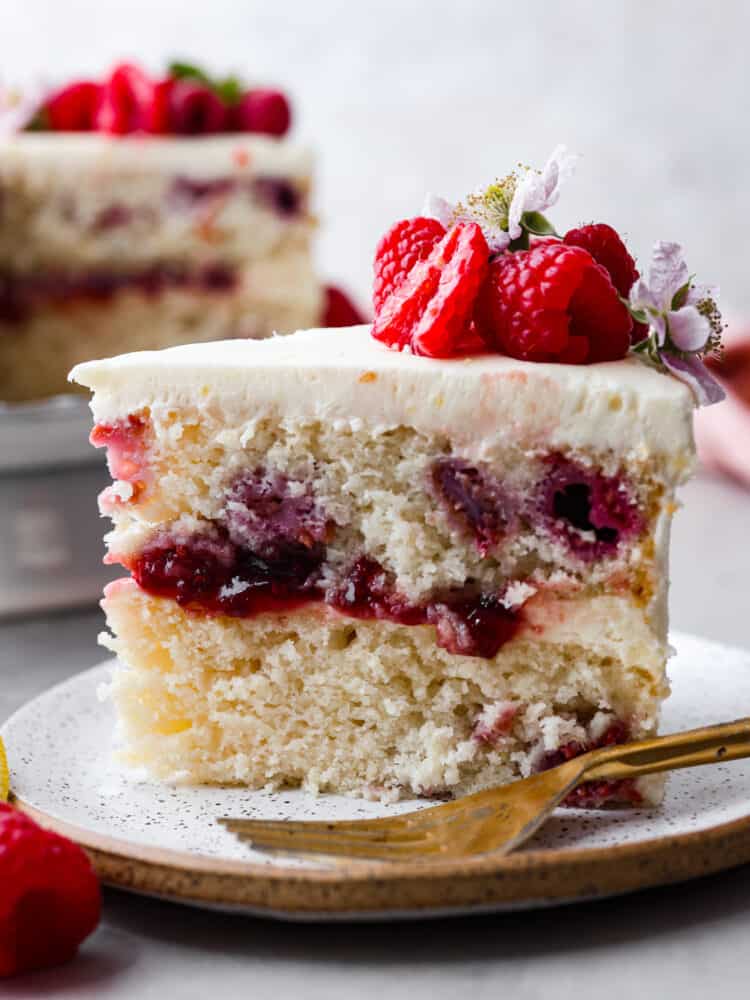 Introducing the ultimate summer dessert: lemon raspberry cake! Zesty lemon layers, juicy raspberries, and creamy lemon frosting make this a must-try dessert. It's impressive, delicious, and everyone will want a slice. Closeup of a slice of lemon raspberry cake.