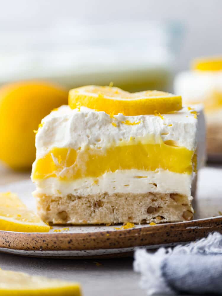 This lemon lush dessert has a delectable combination of flavors. Its buttery pecan crust serves as a delightful base, complementing the refreshing layers of creamy lemon goodness above. It's the best way to stay cool and satisfy your sweet tooth! Closeup of a slice of lemon lush.