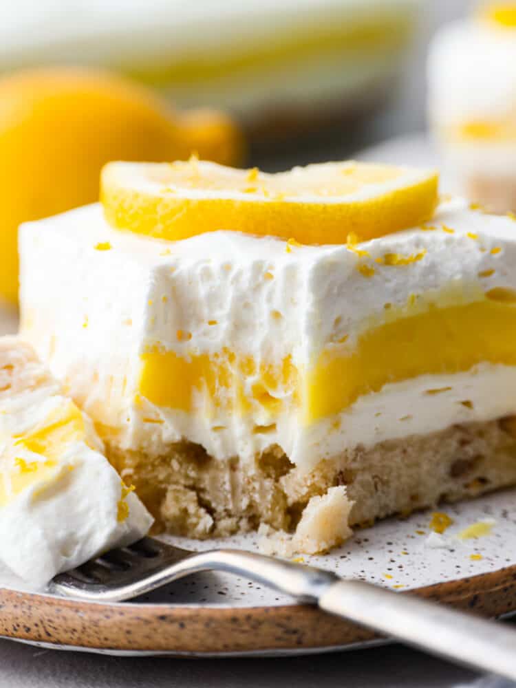 This lemon lush dessert has a delectable combination of flavors. Its buttery pecan crust serves as a delightful base, complementing the refreshing layers of creamy lemon goodness above. It's the best way to stay cool and satisfy your sweet tooth! Closeup of a slice of lemon lush with a bite taken out of it.