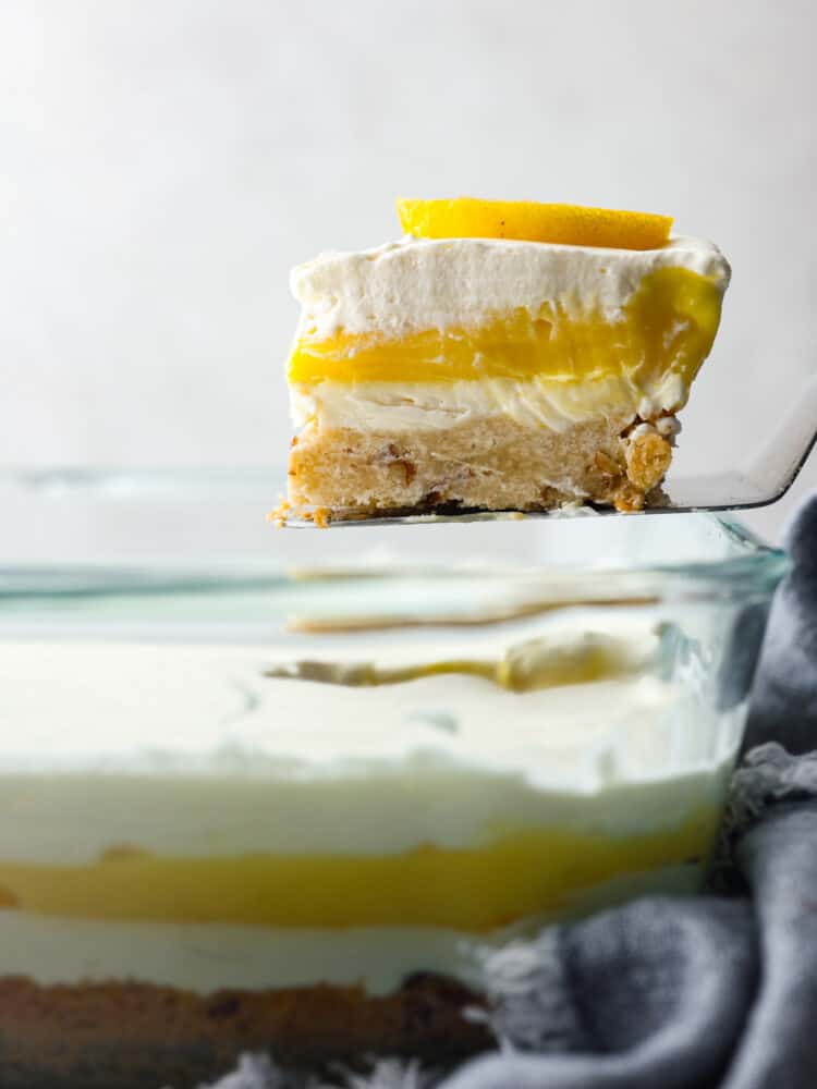 This lemon lush dessert has a delectable combination of flavors. Its buttery pecan crust serves as a delightful base, complementing the refreshing layers of creamy lemon goodness above. It's the best way to stay cool and satisfy your sweet tooth! A slice of the dessert being served with a cake spatula.