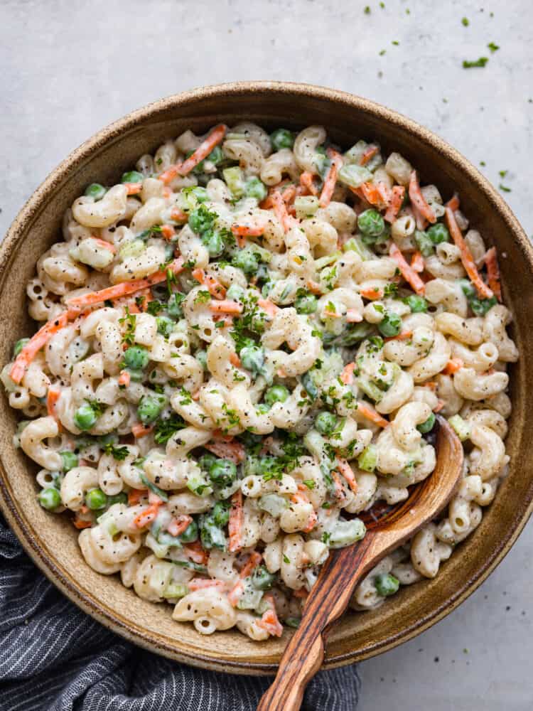 This easy macaroni salad is a potluck superstar! It's creamy and flavorful with peas, carrots, and celery added in for some extra color and crunch. Each bite is a dream! Top-down view of macaroni salad in a wooden bowl.