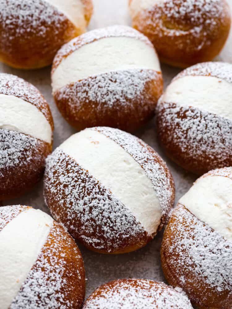 These airy, cream-filled pastries are called maritozzi and a must-make for any dessert lover. The buns have a soft, tender texture that pairs perfectly with the luscious vanilla filling! Top them off with a dusting of powdered sugar for a sweet Italian treat that everyone will love. Top-down view of maritozzi, cream-filled buns.
