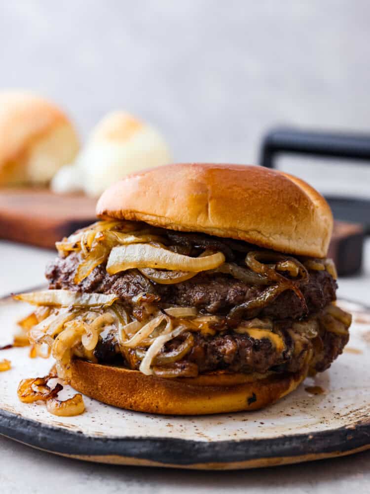 Oklahoma fried onion burgers are packed with so much flavor, thanks to each patty being stamped with heaps of sweet and savory caramelized onions! With how easy to make and delicious they are, you wonโt want burgers any other way. An onion smash burger on a stoneware plate.
