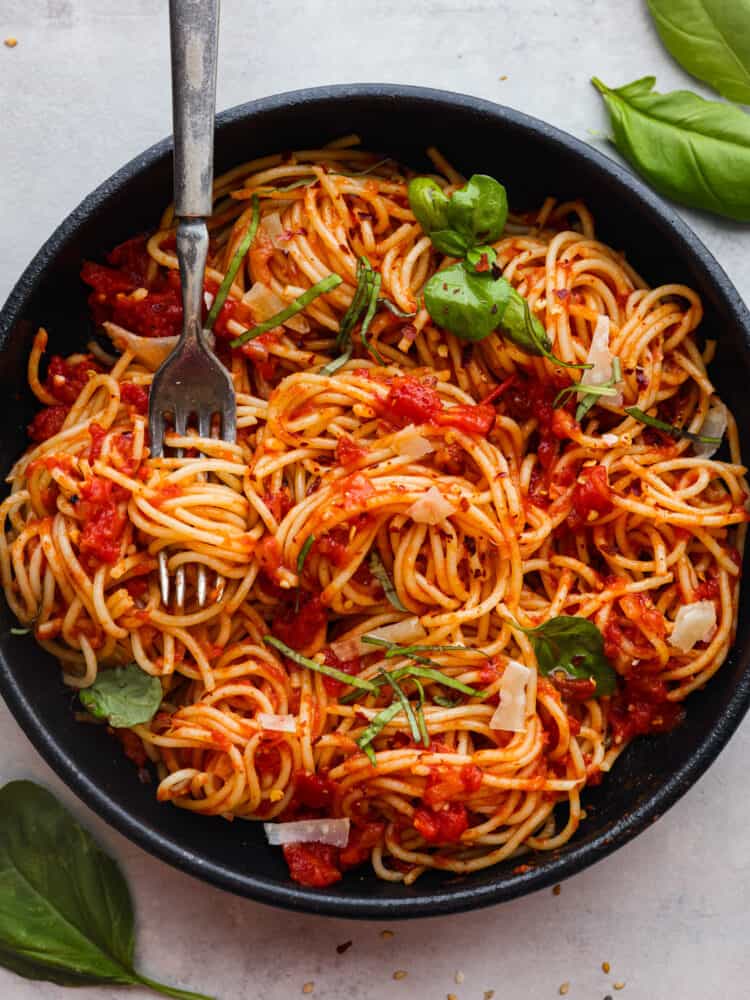 Experience the delicious taste of Italy with this easy Pasta Pomodoro recipe. Cook the pasta and make a flavorful tomato sauce with shallots, garlic, and a hint of red pepper flakes. Top it off with melted parmesan cheese and fresh basil for a mouthwatering dish that will leave you wanting more! A bowl of pasta pomodoro with a fork in it.