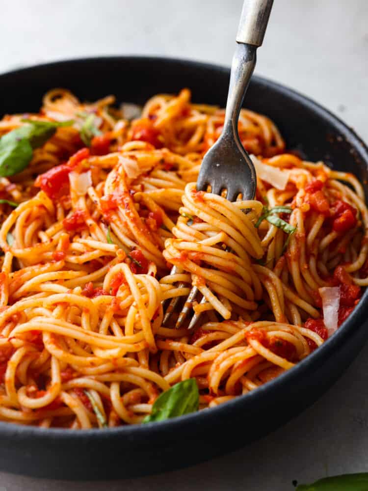 Experience the delicious taste of Italy with this easy Pasta Pomodoro recipe. Cook the pasta and make a flavorful tomato sauce with shallots, garlic, and a hint of red pepper flakes. Top it off with melted parmesan cheese and fresh basil for a mouthwatering dish that will leave you wanting more! A close up of pasta wrapped around.a fork in a bowl.
