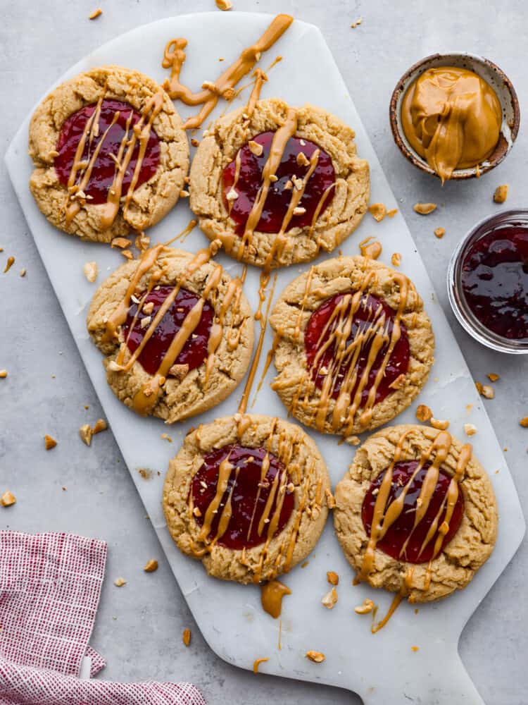 A classic flavor pairing, but in cookie form! These peanut butter and jelly cookies are extra soft and delicious, each with a strawberry jam core and peanut butter drizzle on top. 6 peanut butter and jelly cookies on a stone slab.
