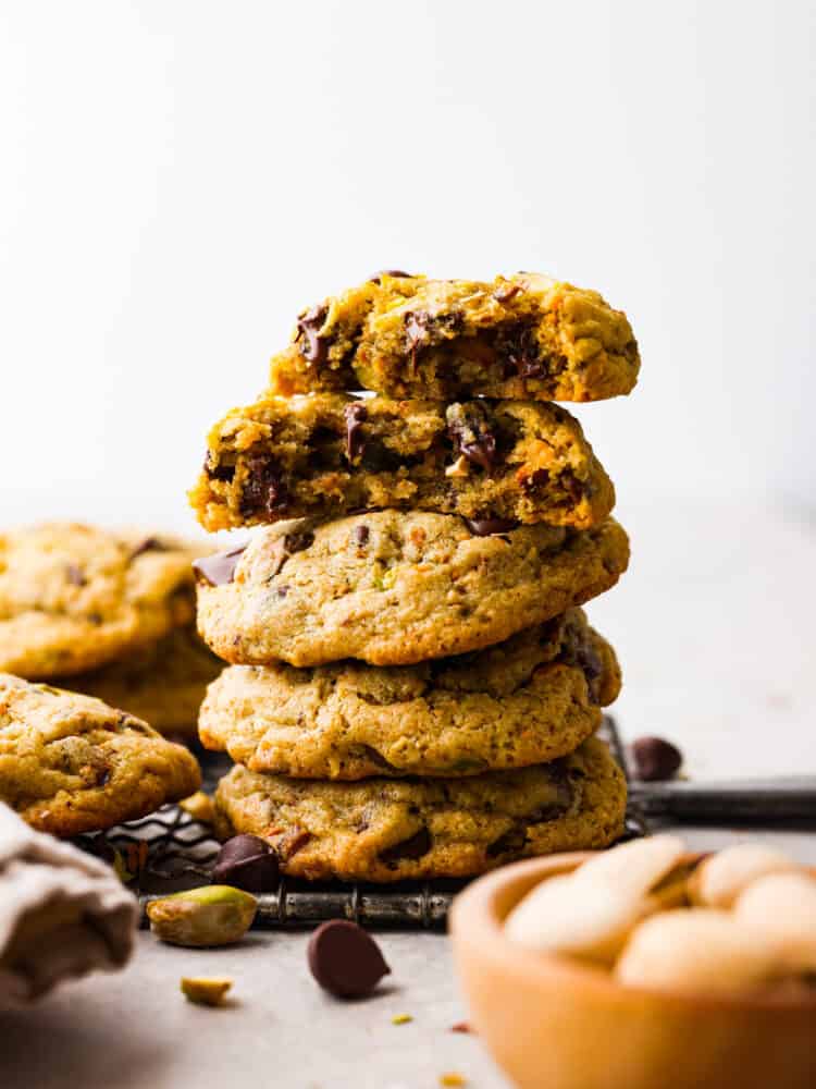 Nutty, sweet, and soft, these chocolate chip pistachio cookies are a must-try dessert! They're super easy to whip up and absolutely irresistible. A stack of 4 cookies, with one broken in half.