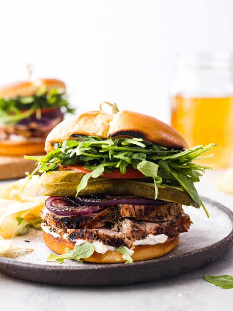 A homemade pork tenderloin sandwich is the perfect hearty lunch! A pork tenderloin sandwich topped with pickles, tomatoes, greens, and grilled onions.