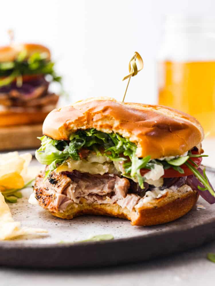 A homemade pork tenderloin sandwich is the perfect hearty lunch! Front view of a sandwich with a bite taken out of it.