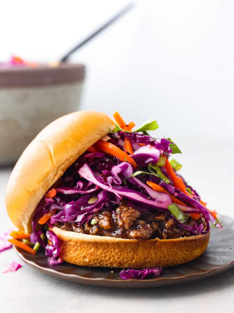 Who would've thought that red cabbage slaw could be so dang tasty? Trust me, this stuff is delicious! Finely sliced red cabbage, matchstick carrots, and herbs tossed with a killer dressing made of olive oil, lime juice, honey, and garlic. It’s the perfect way to jazz up any dish. Red cabbage slaw served on a sandwich.