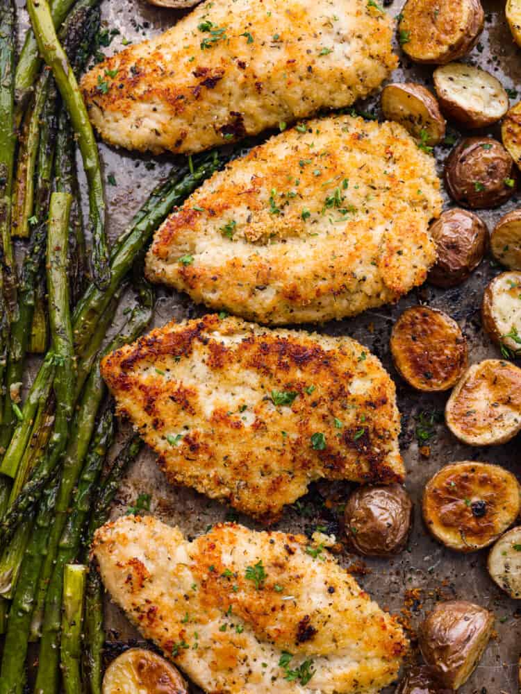 The top view of chicken breasts, asparagus and baby potatoes on a sheet pan.