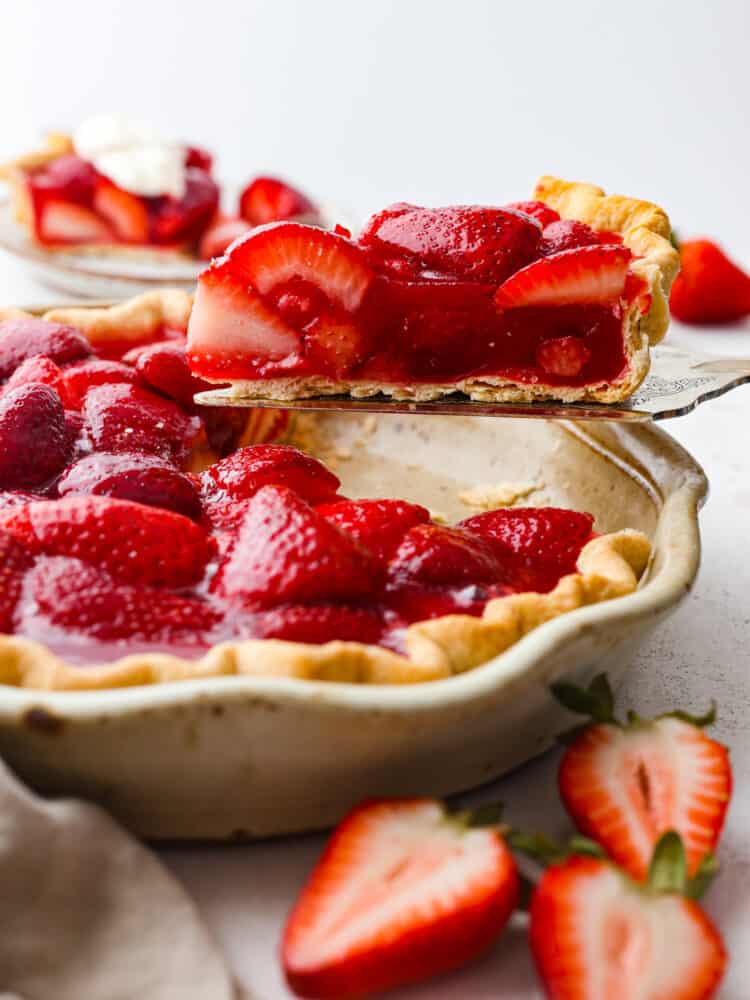 This easy and fresh strawberry pieย features sweet, juicy strawberries, and a flaky, homemade crust all covered in juicy berry glaze. A slice of pie being served with a cake spatula.