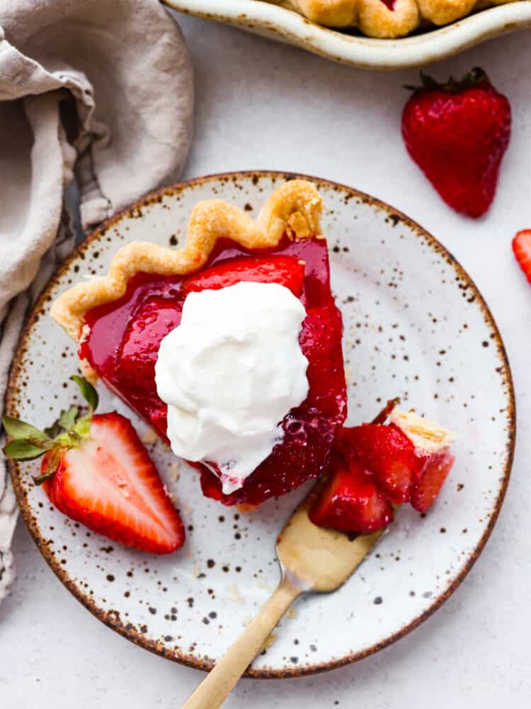 This easy and fresh strawberry pieย features sweet, juicy strawberries, and a flaky, homemade crust all covered in juicy berry glaze. Top-down view of a slice of pie, topped with whipped cream.