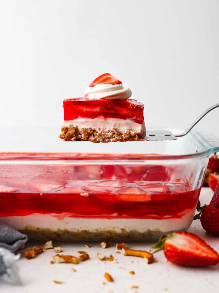 Strawberry Pretzel Salad has a sweet and salty pretzel crust, cream cheese middle, and a jello strawberry layer on top. Perfection!ย Everyone loves this salad! A slice of the strawberry dessert being served.