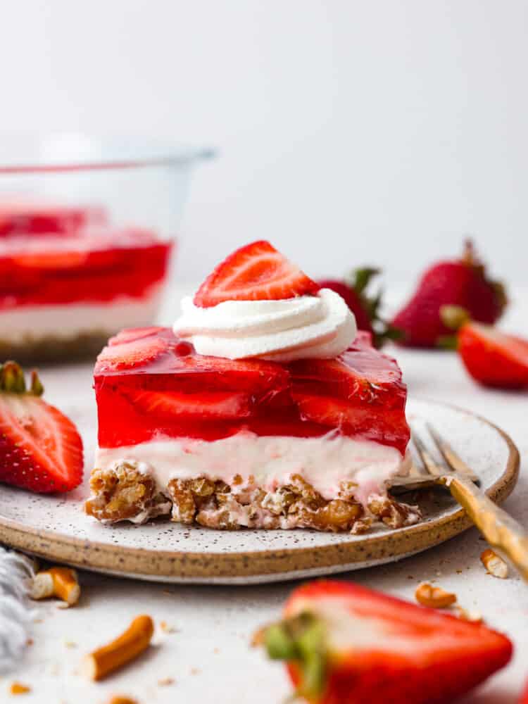Strawberry Pretzel Salad has a sweet and salty pretzel crust, cream cheese middle, and a jello strawberry layer on top. Perfection!ย Everyone loves this salad! A slice of strawberry pretzel salad on a stoneware plate.