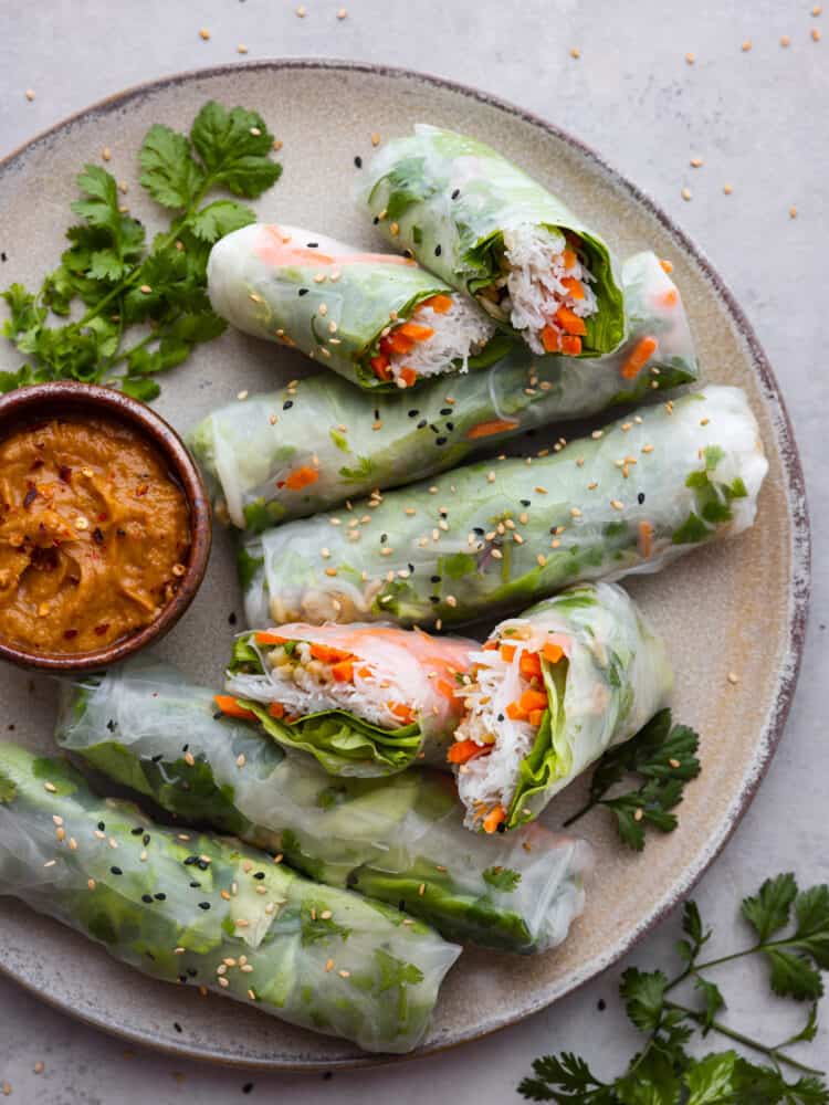 If you're wanting a light and delicious snack, look no further than these Vietnamese summer rolls! They're packed with fresh, crisp veggies and perfect for dipping in your favorite sauces. Vietnamese summer rolls served on a gray stoneware plate alongside peanut sauce for dipping.