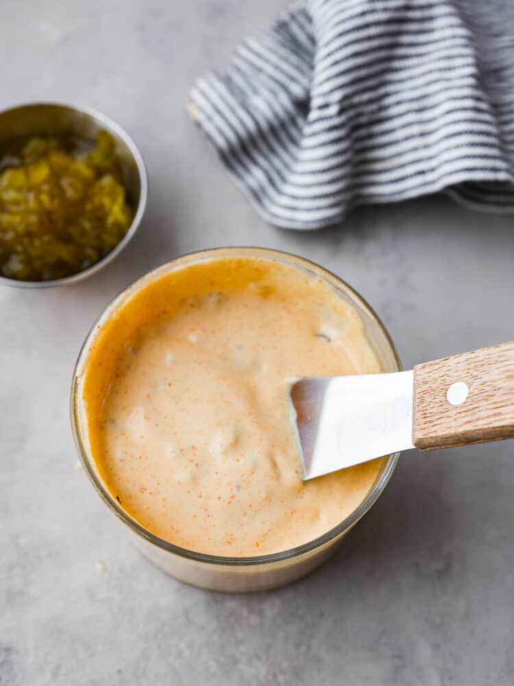 Level up your burgers with this tasty homemade Big Mac sauce! It's made with creamy mayo, pickle relish, vinegar, and a bunch of delicious seasonings. You'll always want it on hand! Top-down view of big mac sauce container with a small serving spatula in it.