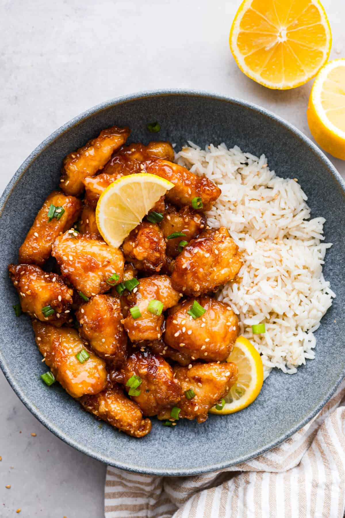 Crispy on the outside, tender on the inside, and covered in a zesty, savory glaze, this Chinese lemon chicken is sure to become a new dinnertime favorite. It's a better-than-takeout meal the whole family will go crazy over! Lemon chicken served with rice in a gray stoneware bowl.