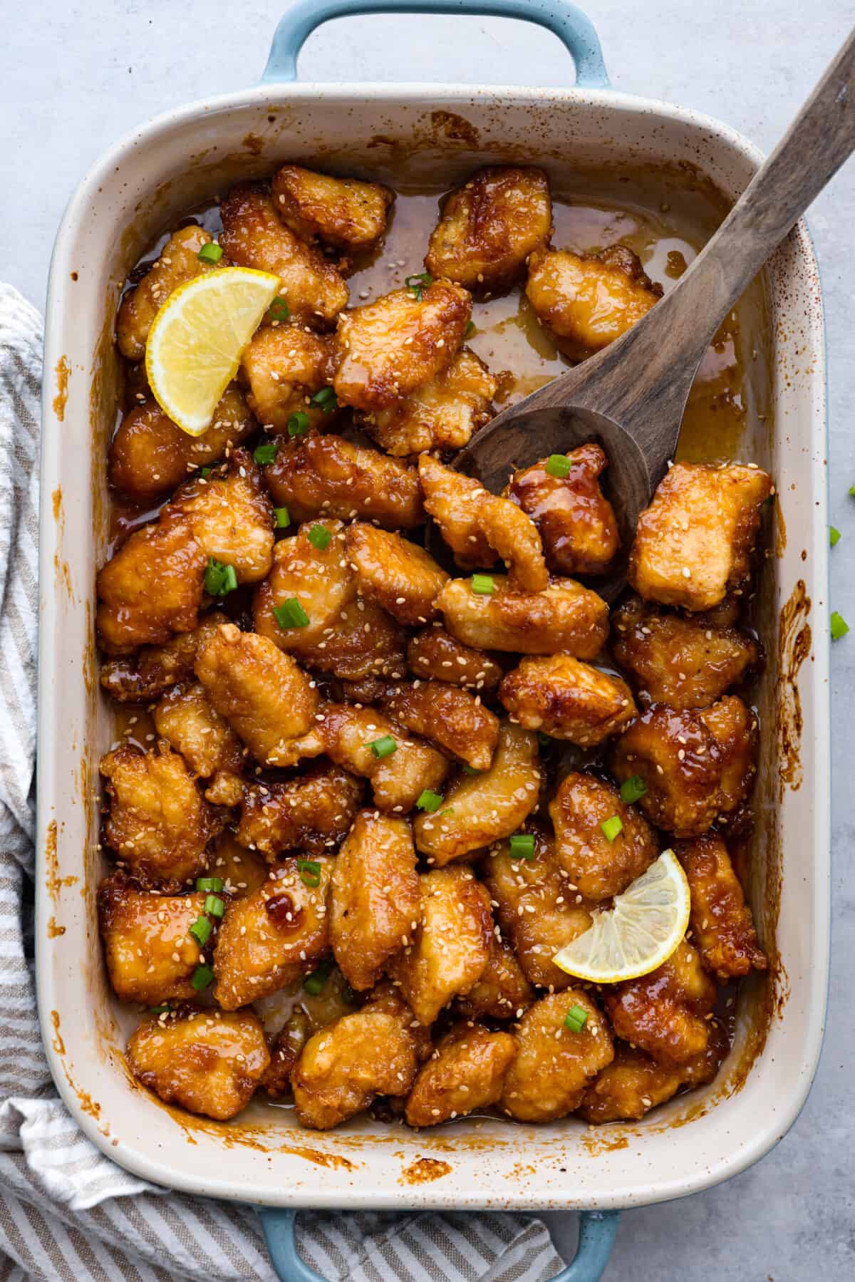 Crispy on the outside, tender on the inside, and covered in a zesty, savory glaze, this Chinese lemon chicken is sure to become a new dinnertime favorite. It's a better-than-takeout meal the whole family will go crazy over! Chinese lemon chicken in a blue and white casserole dish.