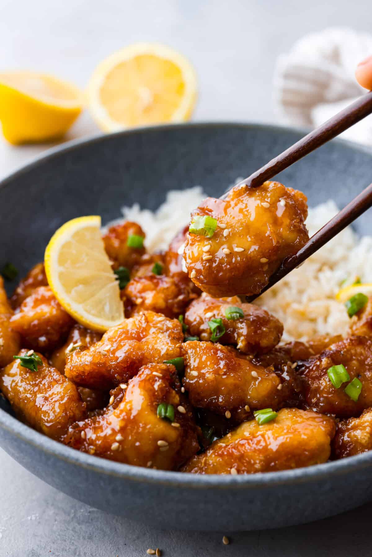 Crispy on the outside, tender on the inside, and covered in a zesty, savory glaze, this Chinese lemon chicken is sure to become a new dinnertime favorite. It's a better-than-takeout meal the whole family will go crazy over! A piece of chicken being picked up with chopsticks.