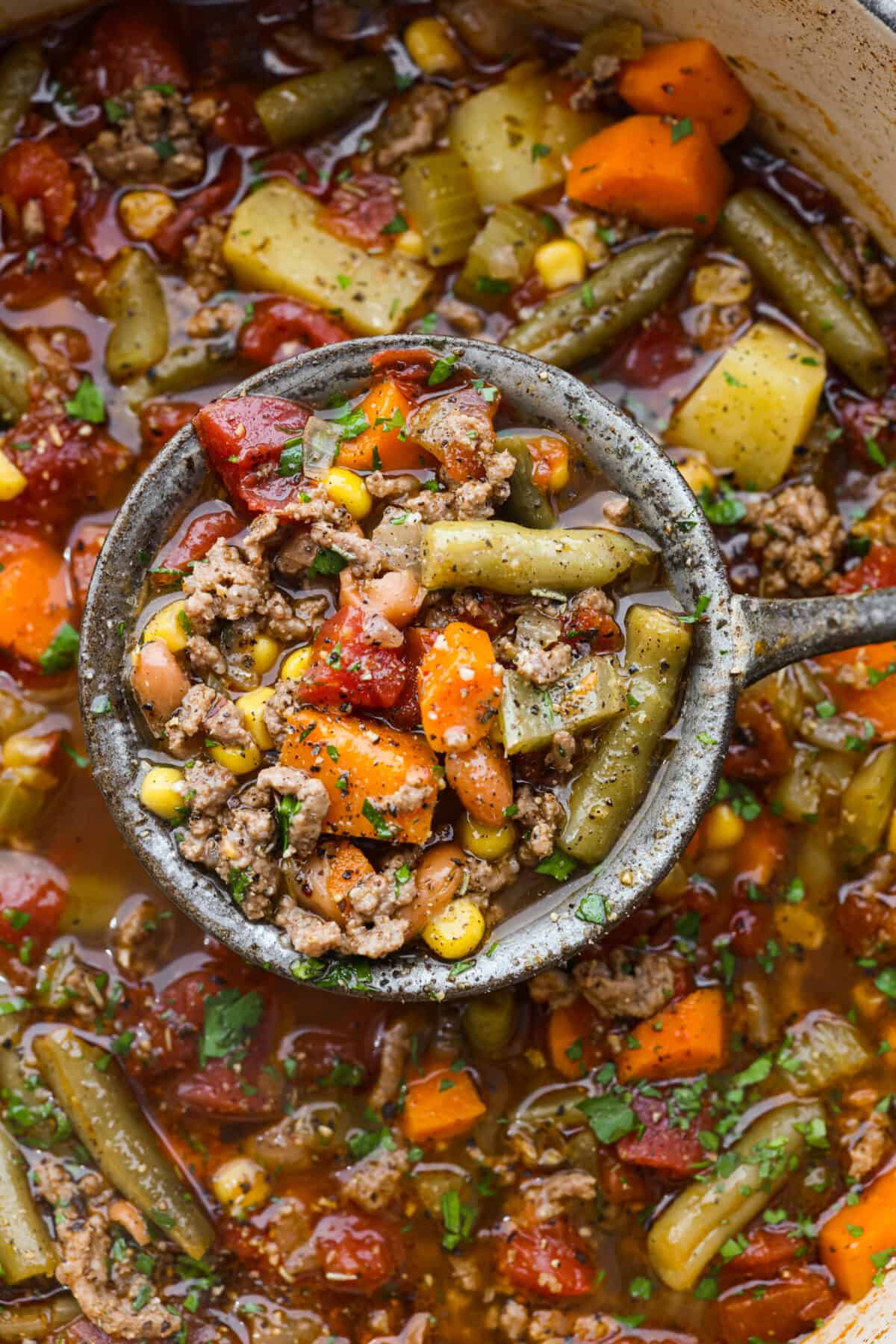 Experience the wild west in a bowl with this Cowboy Hamburger Soup recipe! This comforting blend features seasoned ground beef, veggies, and a touch of Tex-Mex, simmered to perfection in a hearty beef broth. A close up of hamburger soup in a ladle.