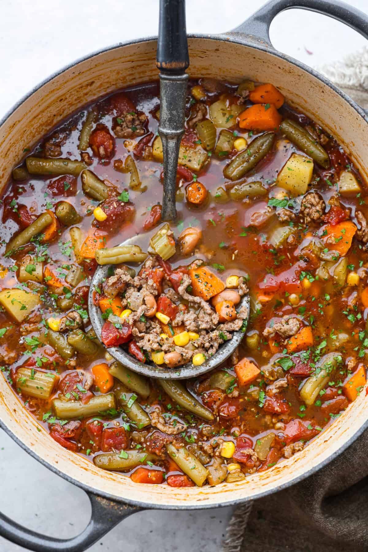 Experience the wild west in a bowl with this Cowboy Hamburger Soup recipe! This comforting blend features seasoned ground beef, veggies, and a touch of Tex-Mex, simmered to perfection in a hearty beef broth. A pot of hamburger soup with a ladle.