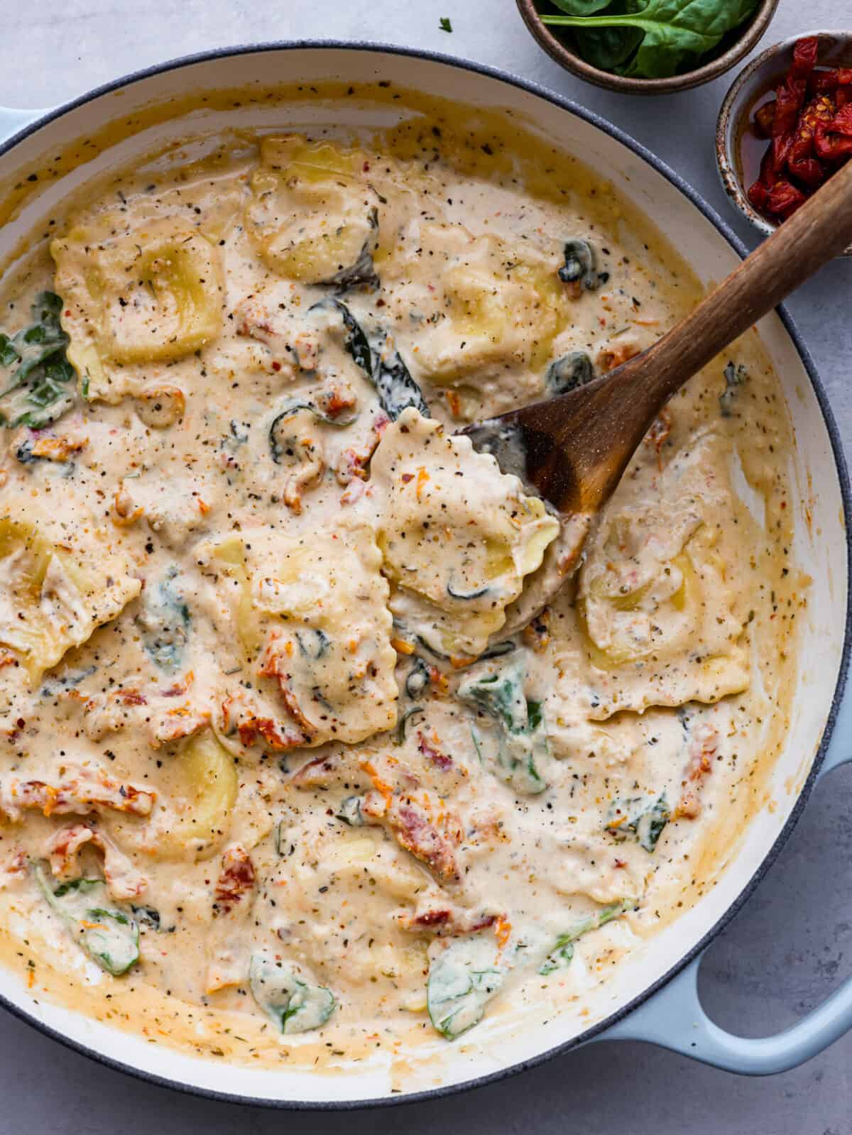 Indulge in this creamy Tuscan ravioli made with the most mouthwatering sun-dried tomato sauce! It's one of the best pasta dishes you'll make, and it's ready in less than 30 minutes. The perfect dinner for busy weeknights! Top-down view of creamy Tuscan ravioli in a blue and white skillet.
