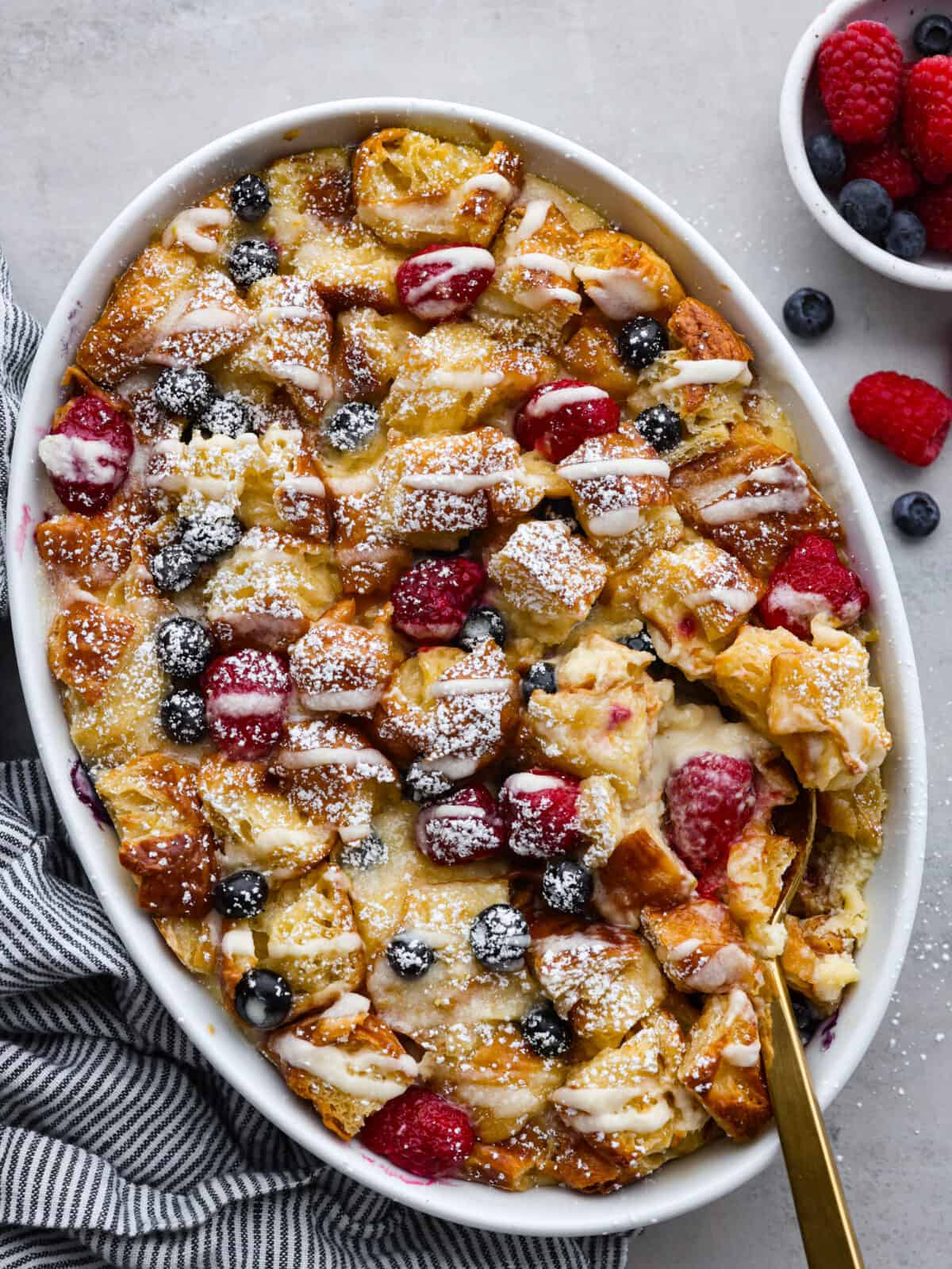 If you love sweet breakfasts, you're in for a treat. This croissant breakfast casserole features tender croissant pieces and fresh berries all coated in a cream cheese custard. As if that's not good enough, everything is topped off with a homemade lemon glaze that's absolutely heavenly. It's love at first bite! Top-down view of a cooked croissant breakfast casserole.